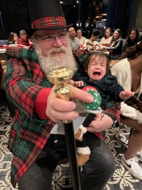 Stage Christmas Party — Jeffry holding a wailing toddler, pointing his cane at the camera, Sun · Dec 17, 2023