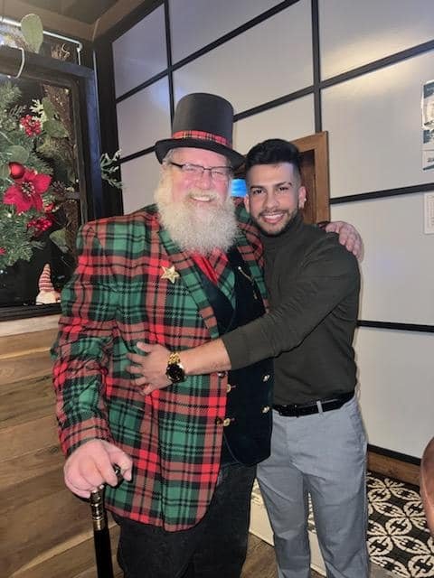 Stage Christmas Party — Jeffry in top hat and plaid jacket with a guest, the poinsettia window behind them, Sun · Dec 17, 2023