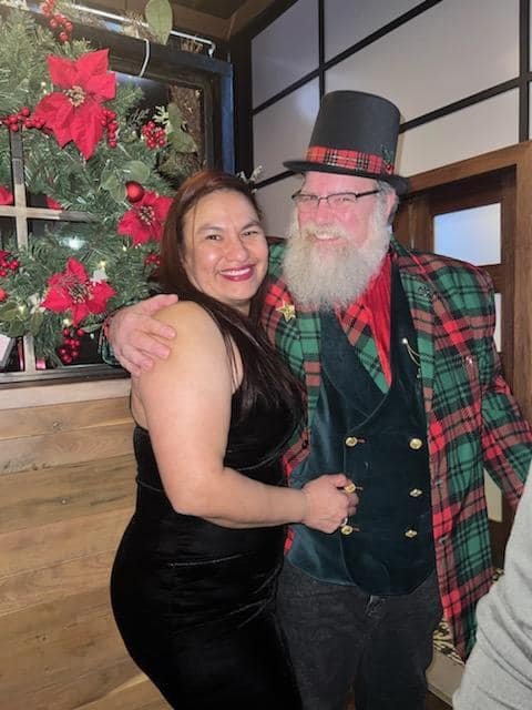 Stage Christmas Party — Jeffry in a plaid jacket with a guest, a poinsettia wreath behind them, Sun · Dec 17, 2023