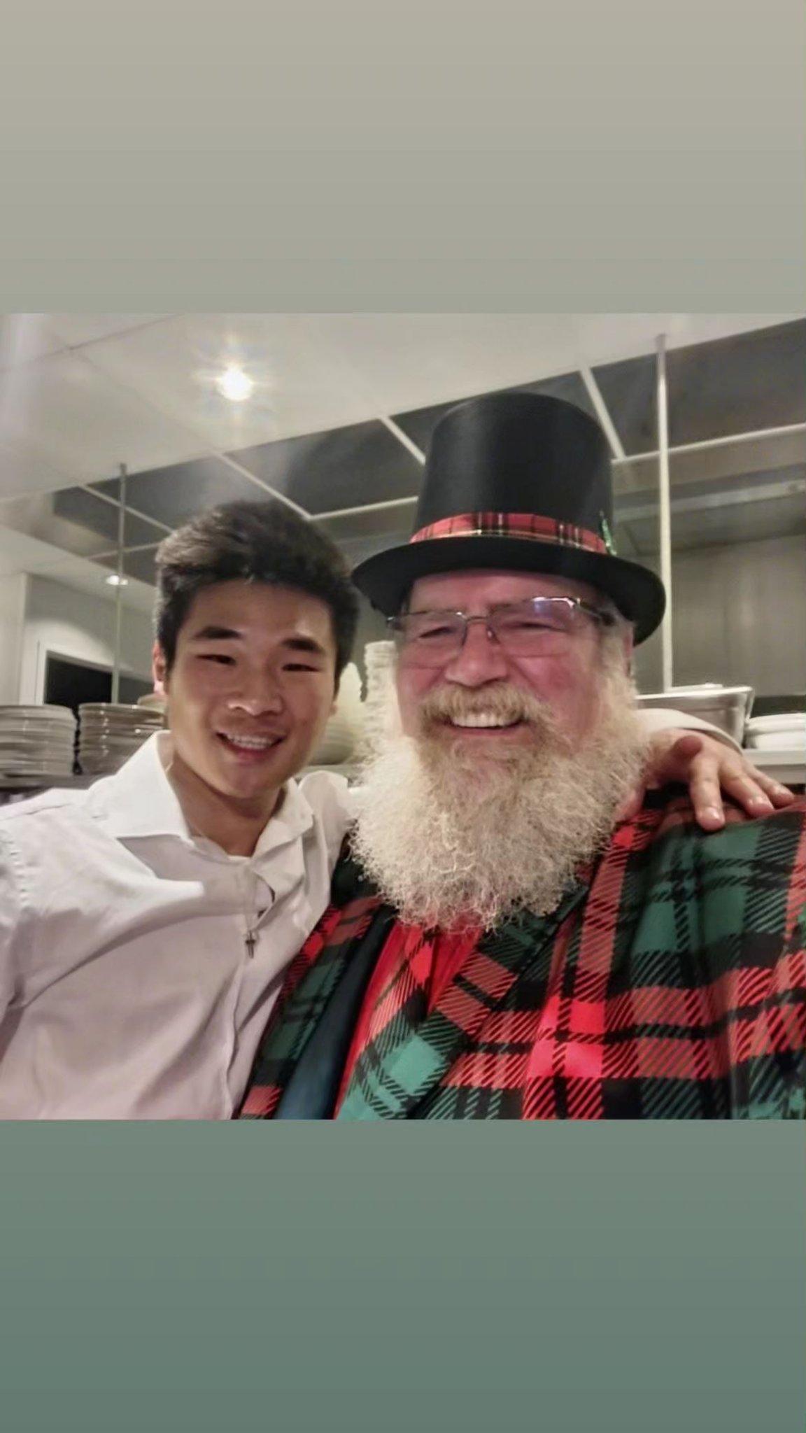 Stage Christmas Party — Jeffry in top hat and plaid jacket with a young member of the Stage team in a white shirt, the kitchen pass behind them, Sun · Dec 17, 2023